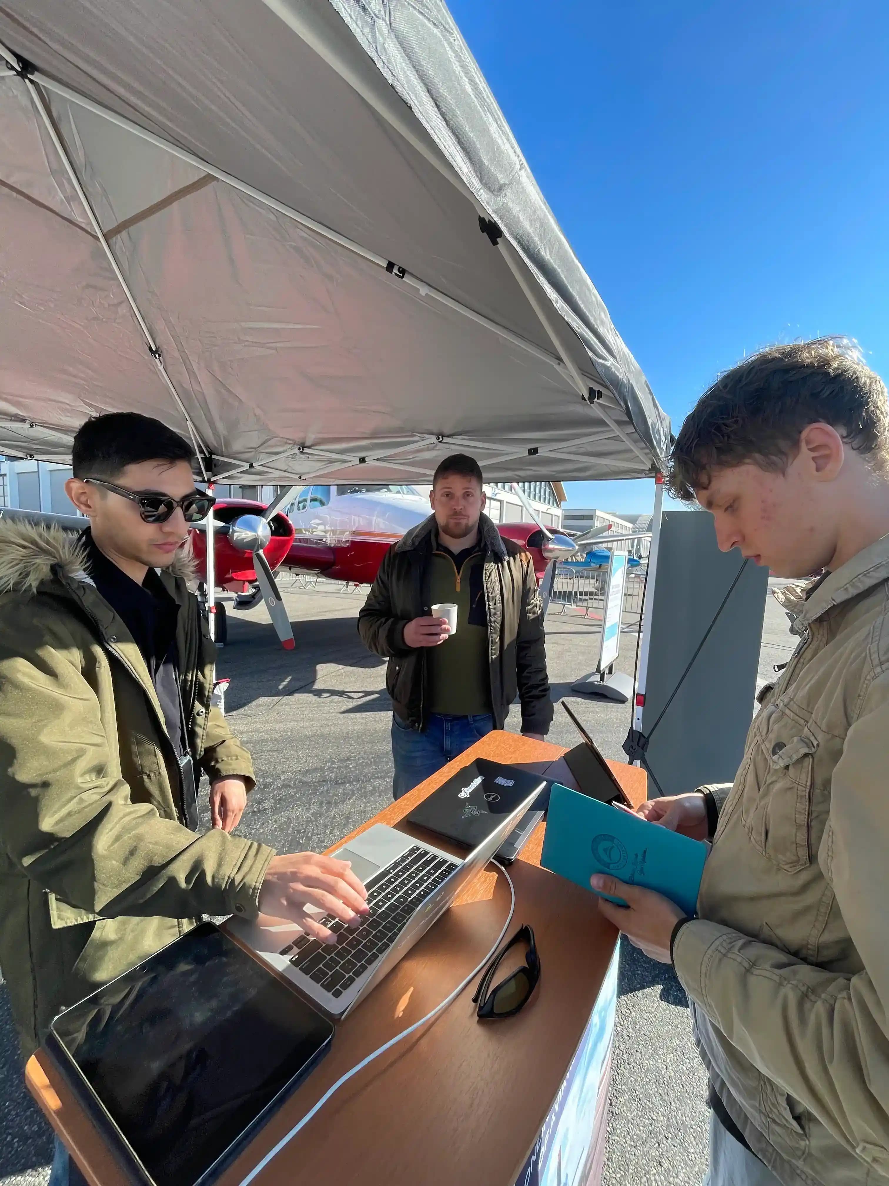 CollectAirs team demonstrating aircraft auction platform on laptops at AERO expo tent