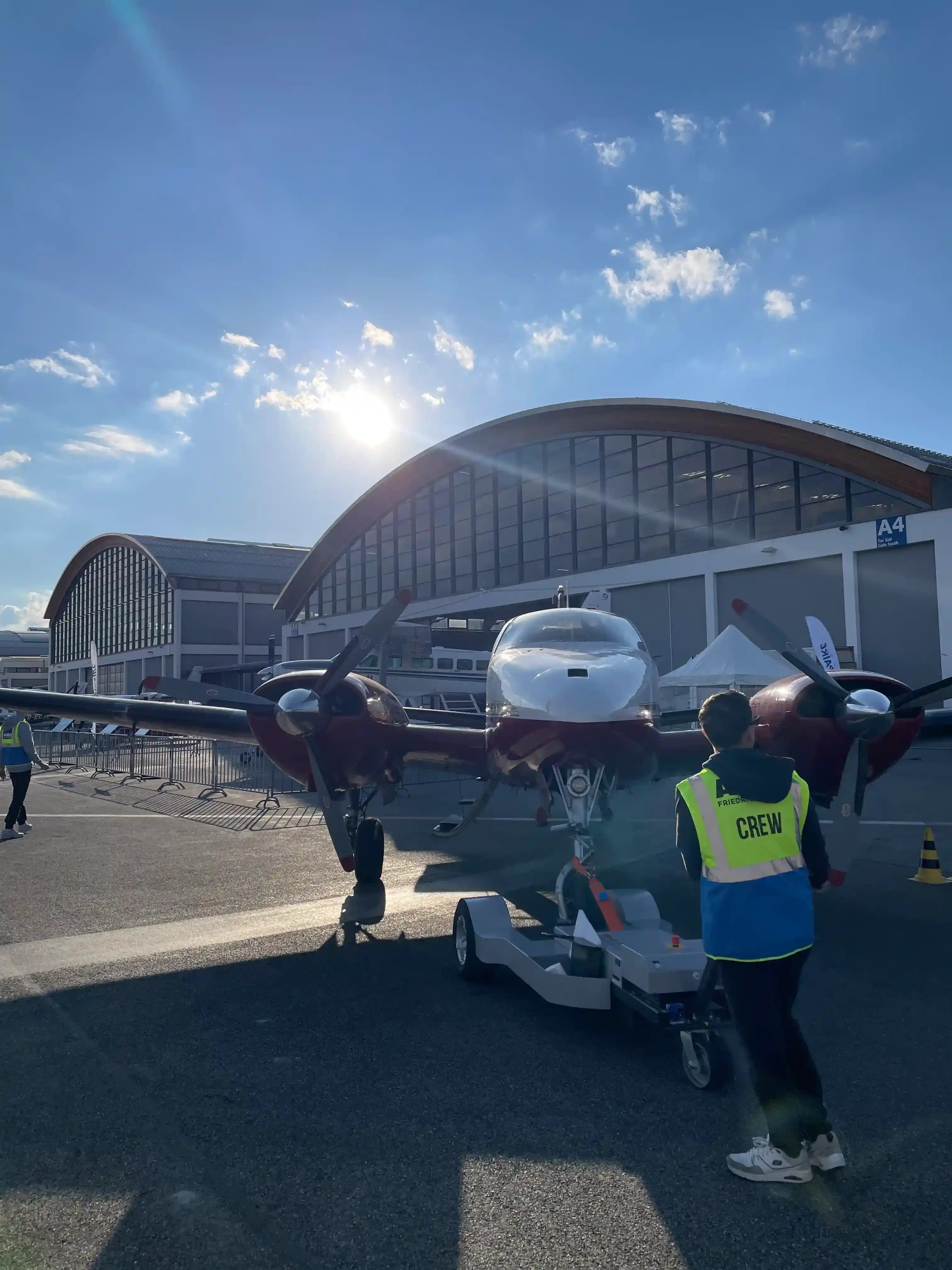 Ground crew towing twin-engine aircraft at AERO Friedrichshafen exhibition halls