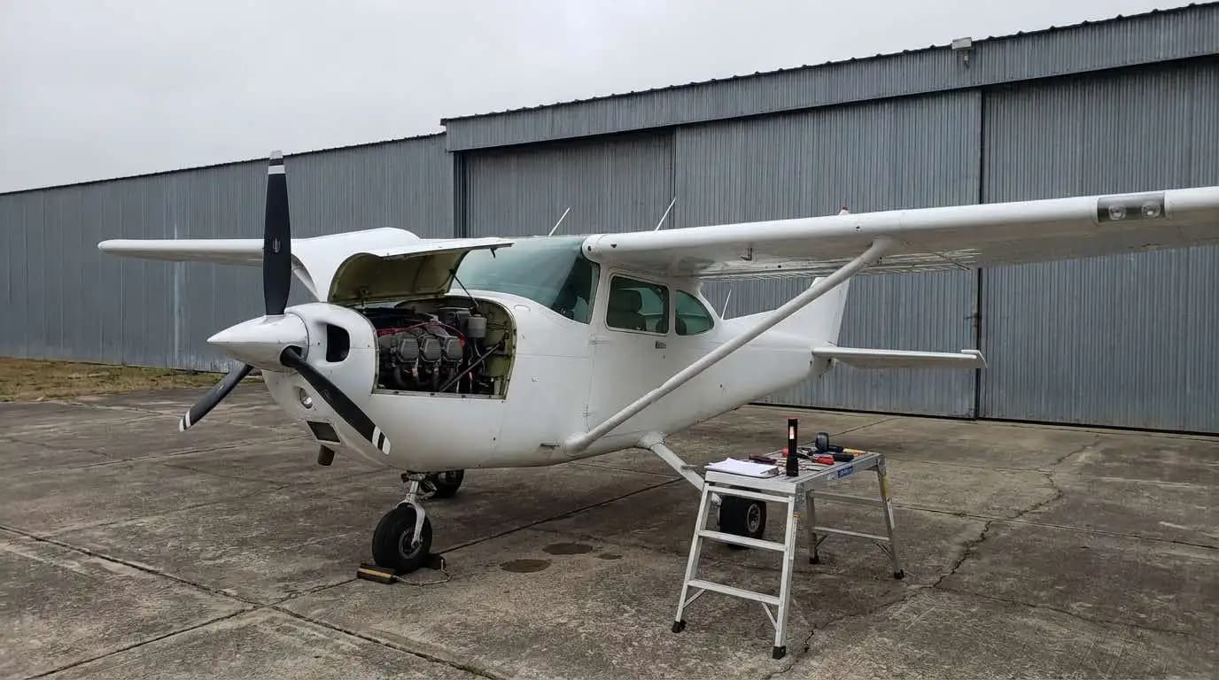 Cessna 182 Skylane parked outside hangar with engine cowling open for inspection