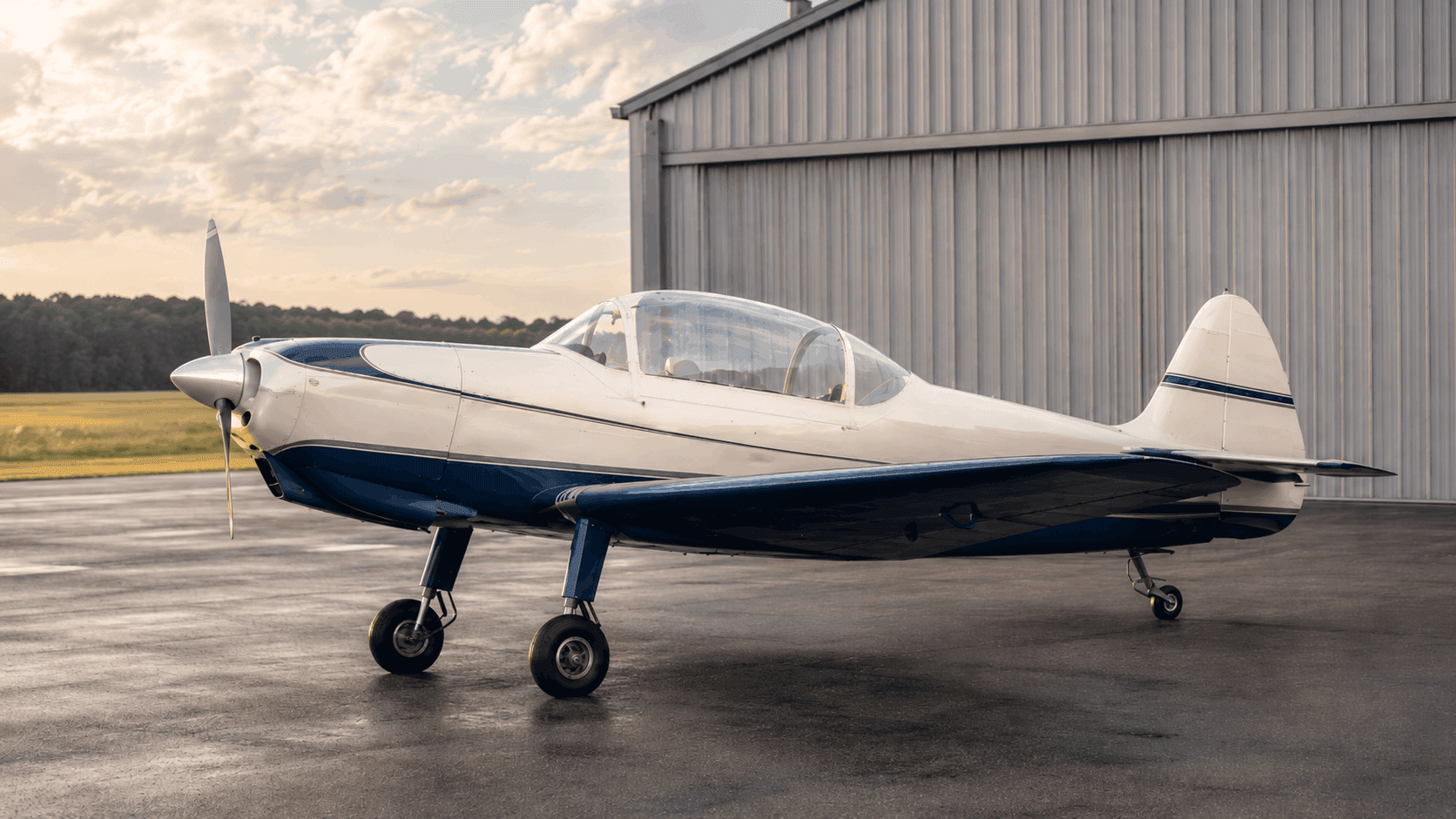 Carefully preserved mid-century two-seat trainer aircraft on a grass airstrip at sunrise
