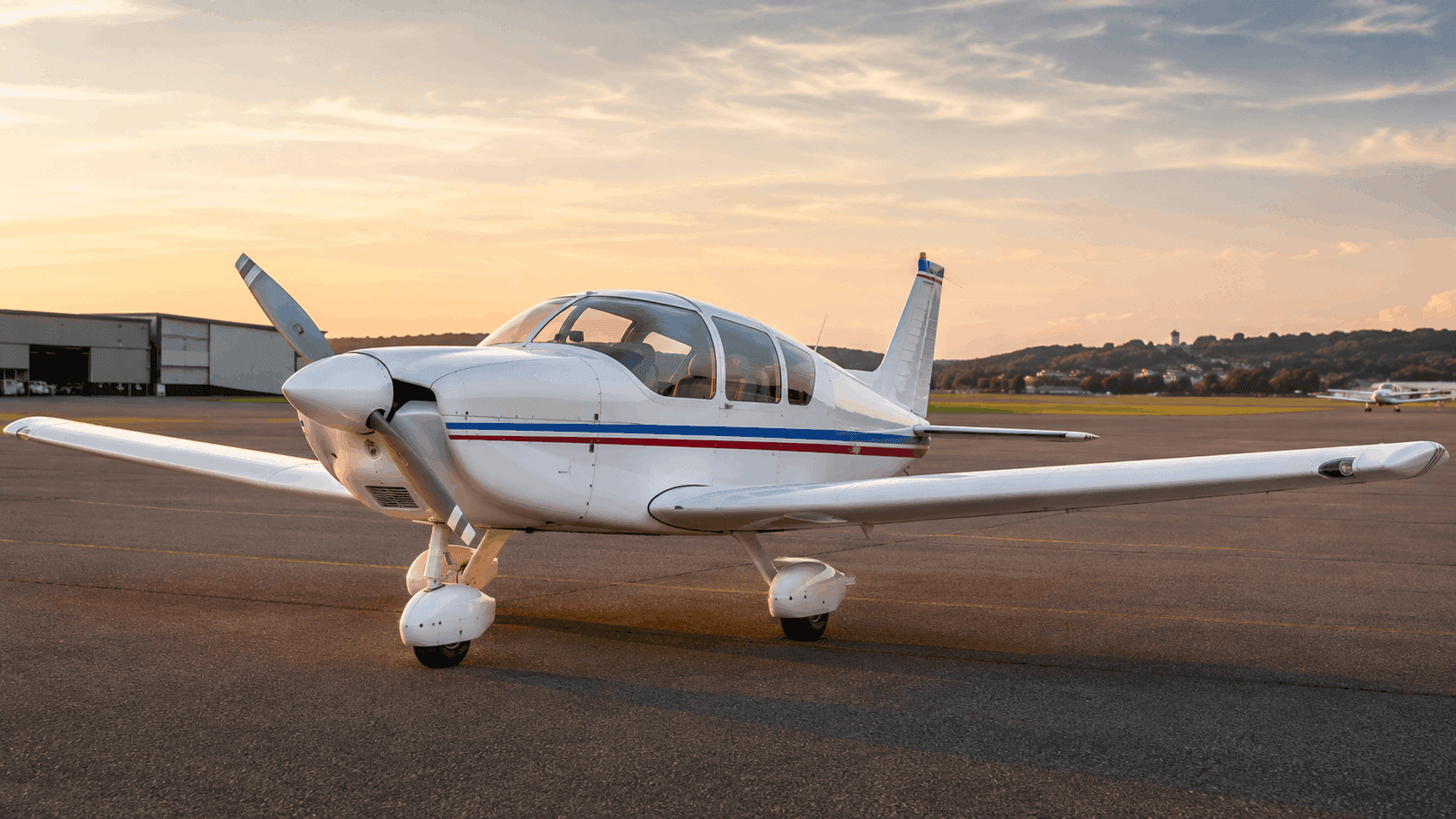 Classic French low-wing wooden touring aeroplane outside a countryside hangar at golden hour
