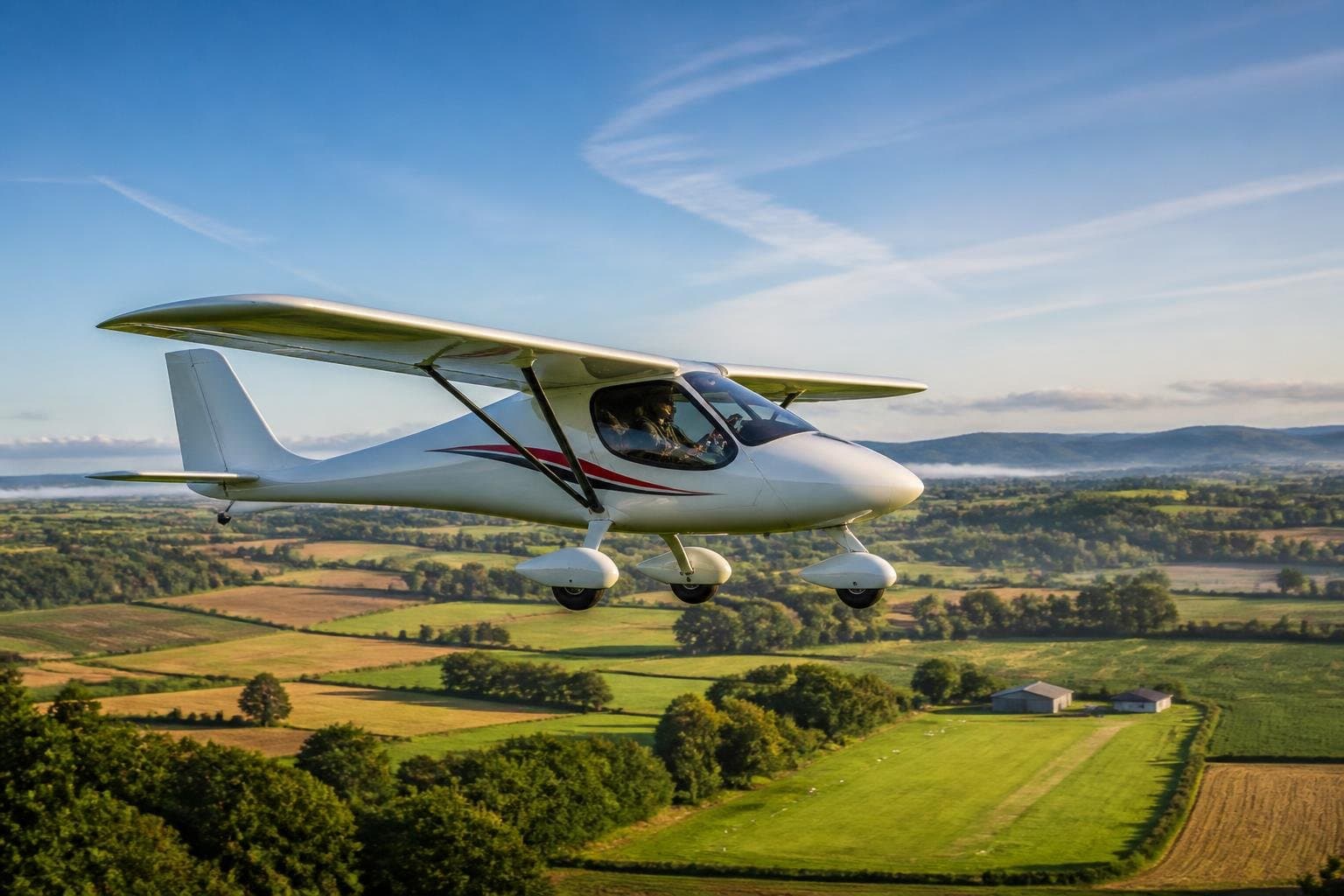 Modern two-seat ultralight aircraft flying over patchwork European farmland near a grass airfield