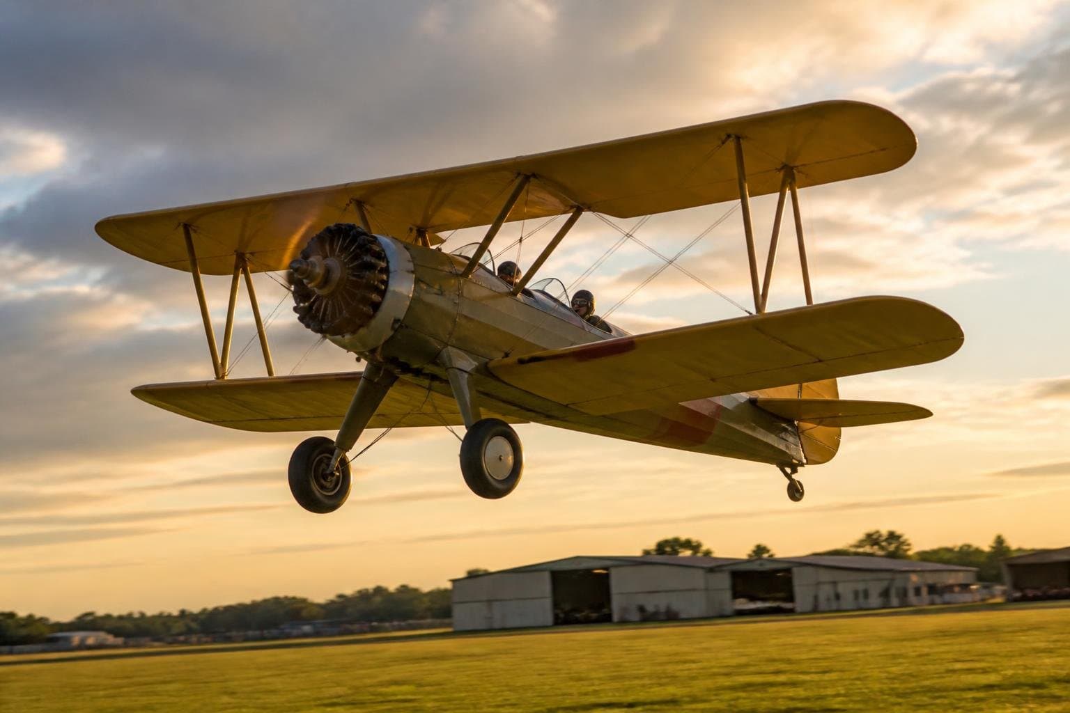 Classic radial-engine biplane trainer climbing above a grass airfield at golden hour